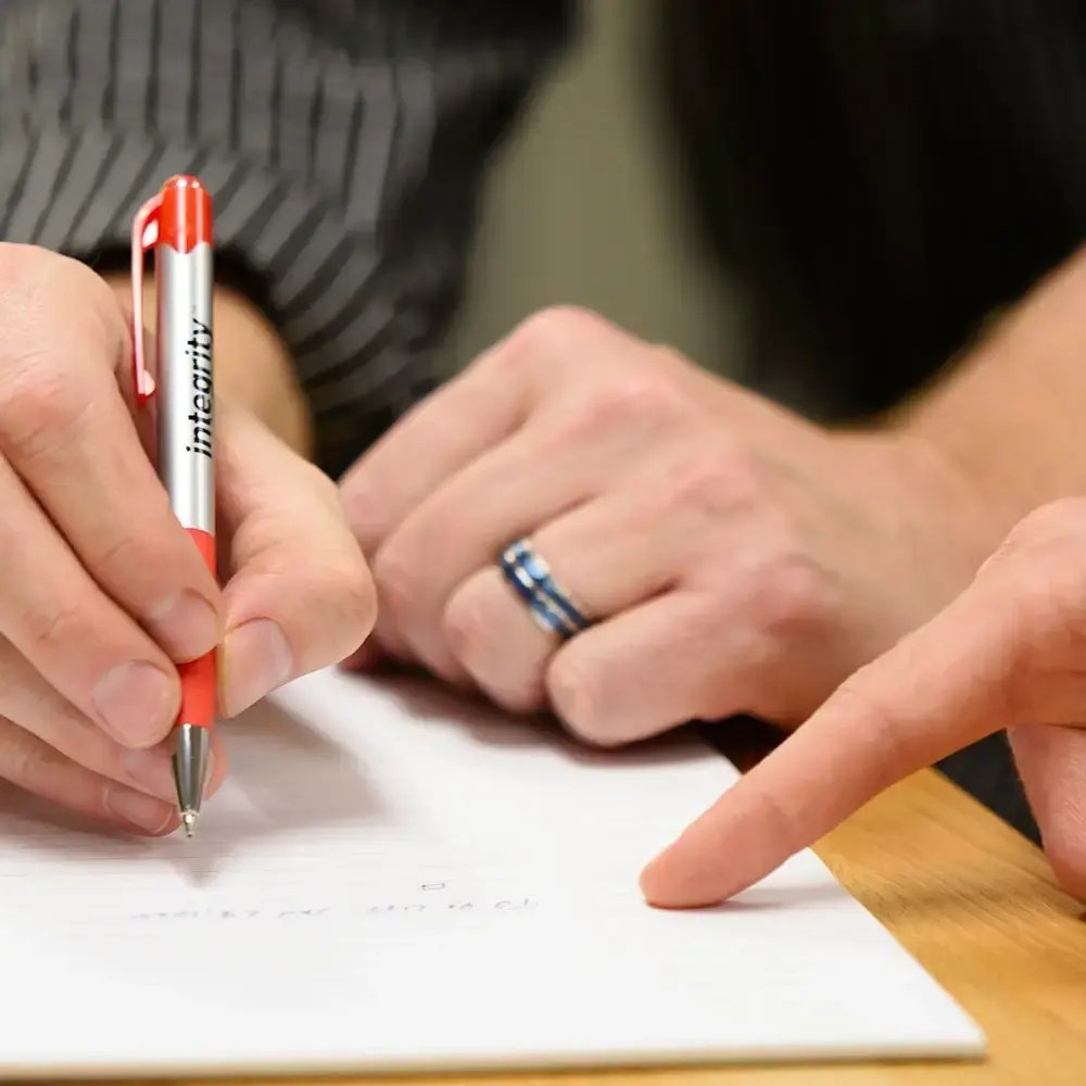 Person writing while another person points at something on the paper