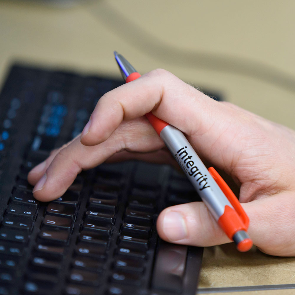 Close up photo of a person holding an Integrity Billing pen and typing on a keyboard